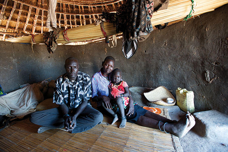 Cezerina Puru Ladu, her husband Garbino and their young daughter sit on a woven mat inside of a round home.