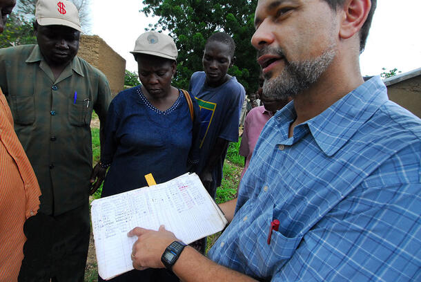 Dr. Frank Richards holds out an open logbook and points at it while speaking to five people.