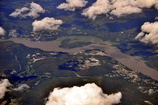An aerial view of the Hudson River and surrounding land below a few clouds.