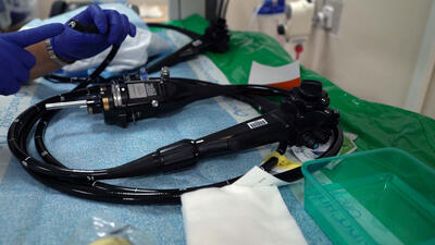 A gloved hand holds one end of a colonoscope, laid out on a table.