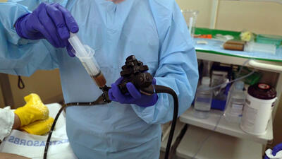 A doctor pushes the stool sample in the syringe into the colonoscopy tube that they're holding.