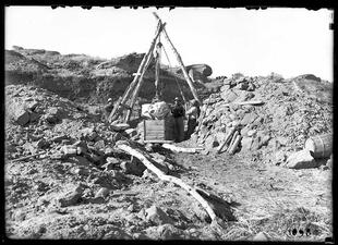 A fossil in a box being lifted out of a site with a pulley system attached to three large sticks creating a conical shape.