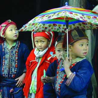 Four young children in colorful dress; one is holding a colorful umbrella.