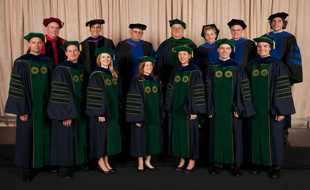 Seated graduates in graduation robes, with scientists and mentors in robes standing behind them.