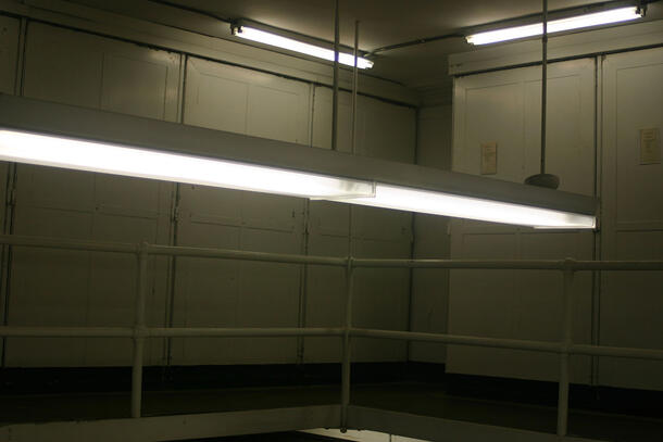 Fluorescent lighting suspended from the ceiling over a dark walkway.