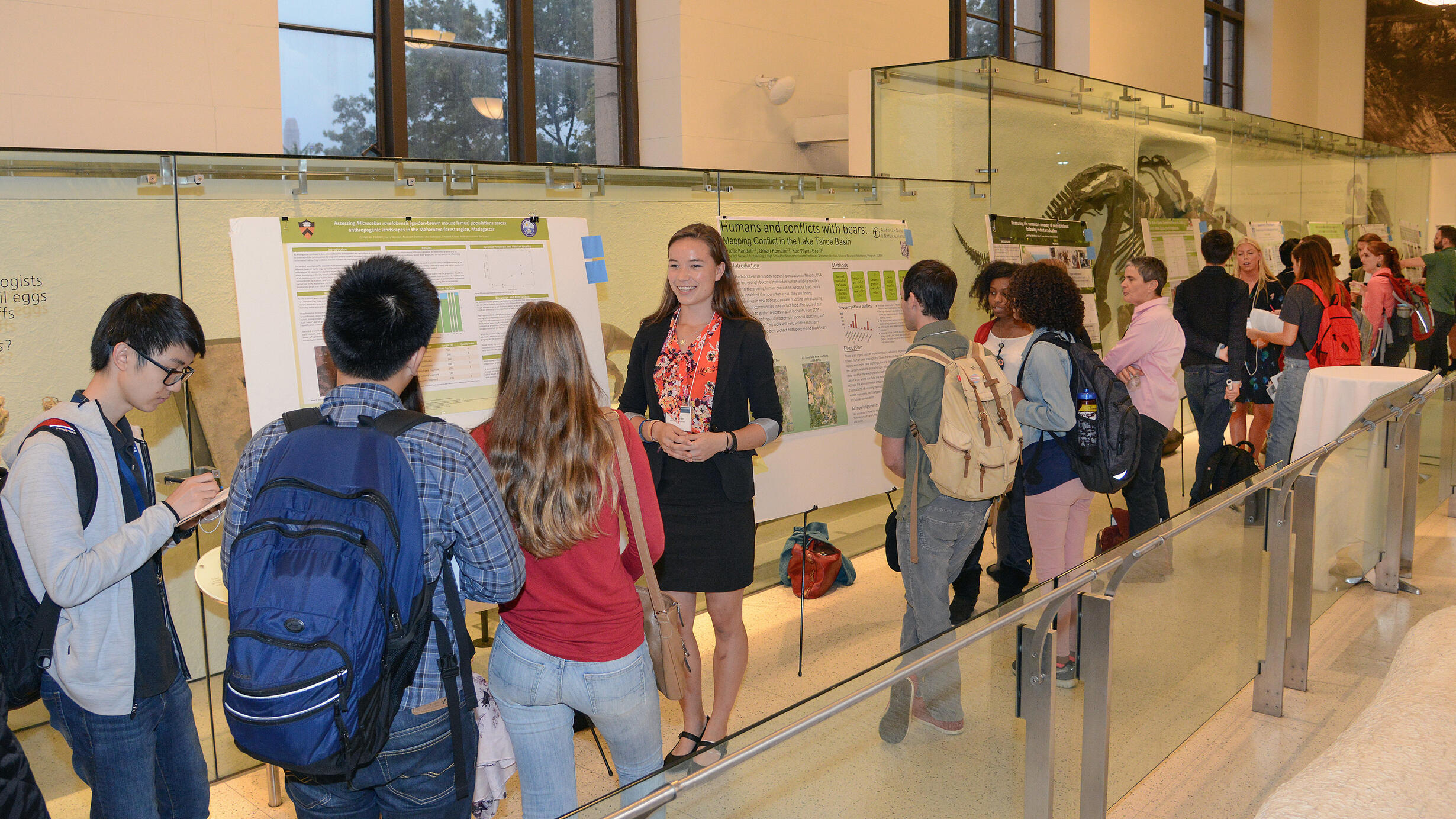 Students stand beside their text-filled poster boards as groups of young people come up to see their presentations.
