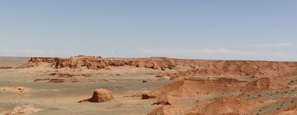 A wide view of Mongolia's Flaming Cliffs, a relatively flat and horizontal mountain range in a desert with a wide sky above.