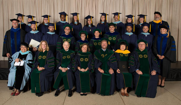 Twenty-eight graduating students in caps and gowns pose in three rows.