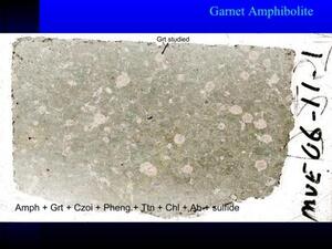 A slide titled "Garnet Amphibolite" with a specimen showing an area of mottled gray color with pink specks and some thin white veining.