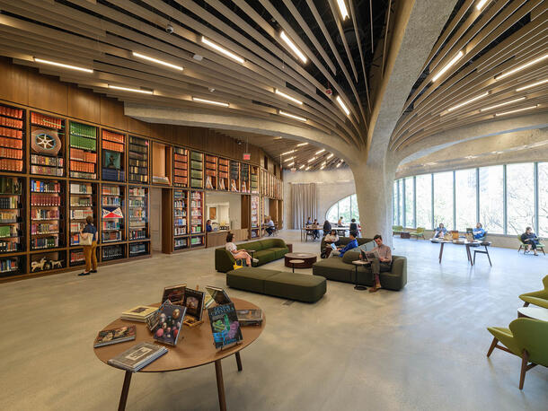Large, open, windowed space lined with bookshelves contains chairs and sofas where visitors are seated and reading.