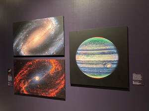 Three large photos on the gallery wall, two depicting spiral galaxies and one depicting Jupiter.