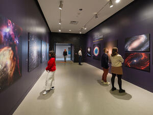 Five visitors stand at various points in the gallery housing Eyes on the Universe looking at large, vivid photographs of space.