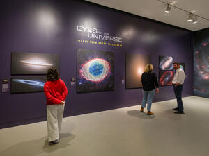 Three visitors stand in front of various large photos of space in the Eyes on the Universe gallery space.