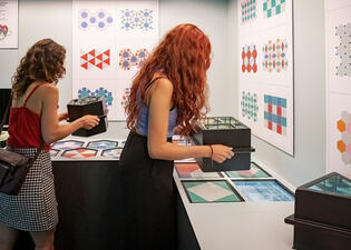 Museum visitors hold viewfinders and look through them at a variety of different mosaics.