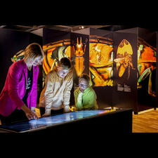 Three people surround a touchscreen kiosk.