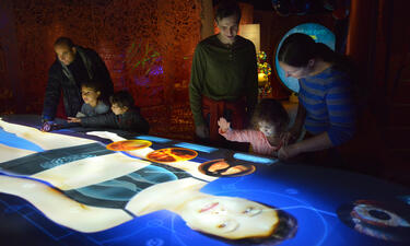 Visitors gather around a 14 foot projection of a woman's body with interactive elements about microbes