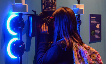 A girl wearing a pink backpack looks through an underwater camera fixed to a wall