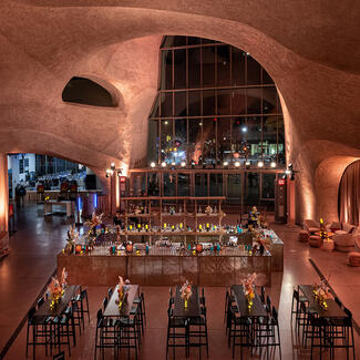 High tables and chairs are placed in front of a large horseshoe-shaped cocktail bar in the dramatically-lit Gilder Center atrium.