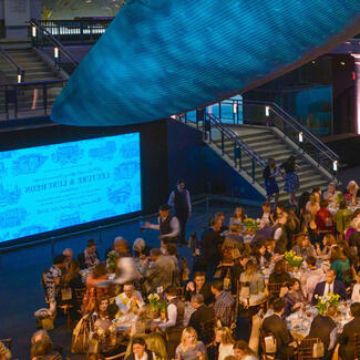 Milstein Hall is filled with guests seated at tables to listen to a panel discussion during the AMNH Science Luncheon for Members.