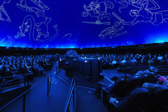 Inside the Hayden Planetarium theater, visitors look upwards at representations of the constellations projected above.