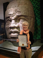 Betty LaBlanc holds her 25 years of service certificate in front of an object in the Museum.