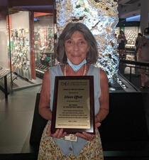 Eileen Effrat stands in the Mignone Halls of Gems and Minerals, and holds a plaque honoring her 40 years of volunteer service.
