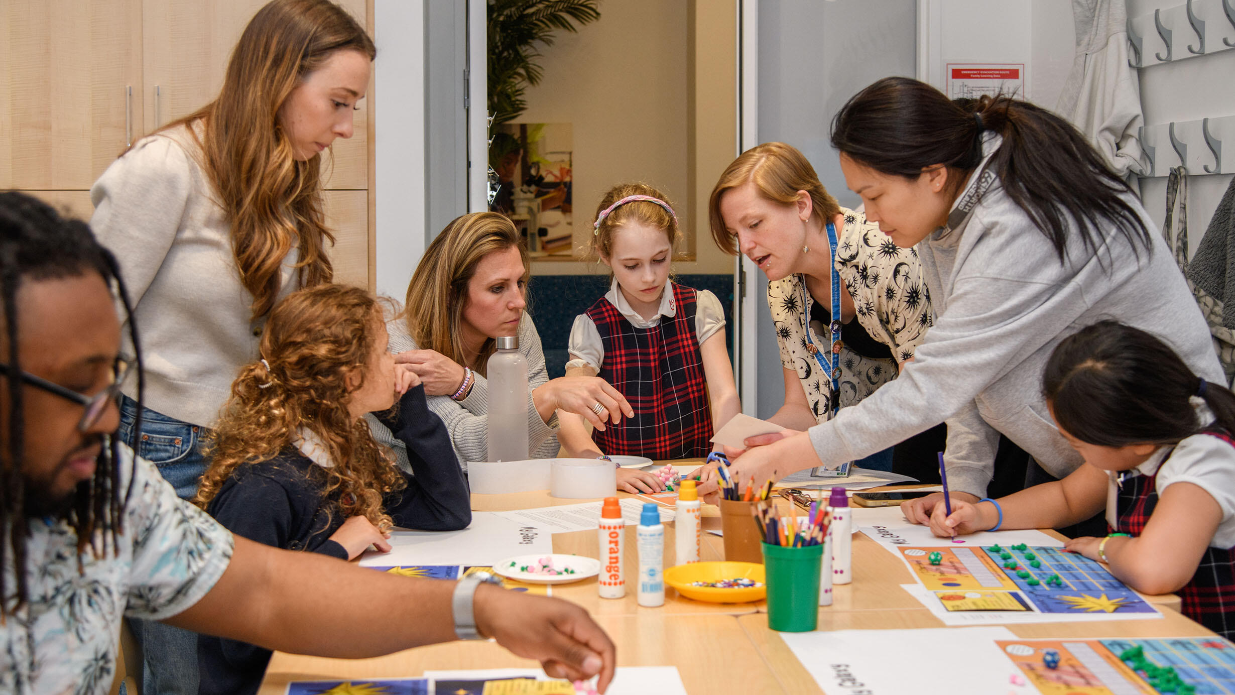 Museum educators gather around a large table containing pencils, glue, and paper to assist children with a creative project.