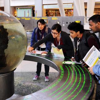 A teacher and four students view the Ecosystem Sphere in the Museum's Hall of the Universe.