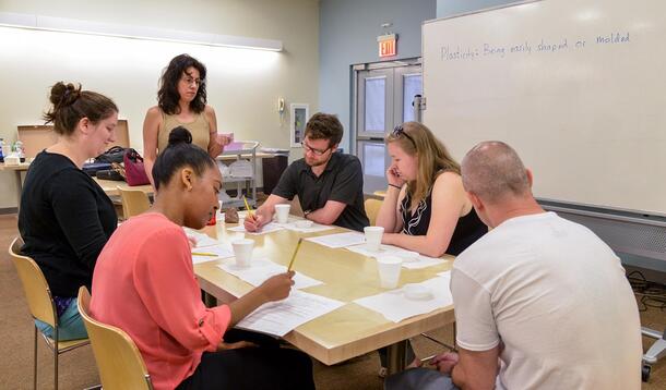 Six alumni of the MAT program sit at a table and compare notes.