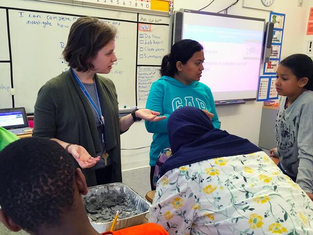 Teacher stands and speaks to four students.