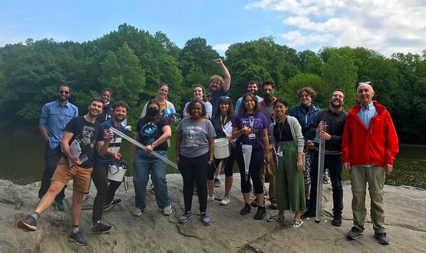 Large group of residents stands with an instructor on a rocky ledge in New York City's Central Park.