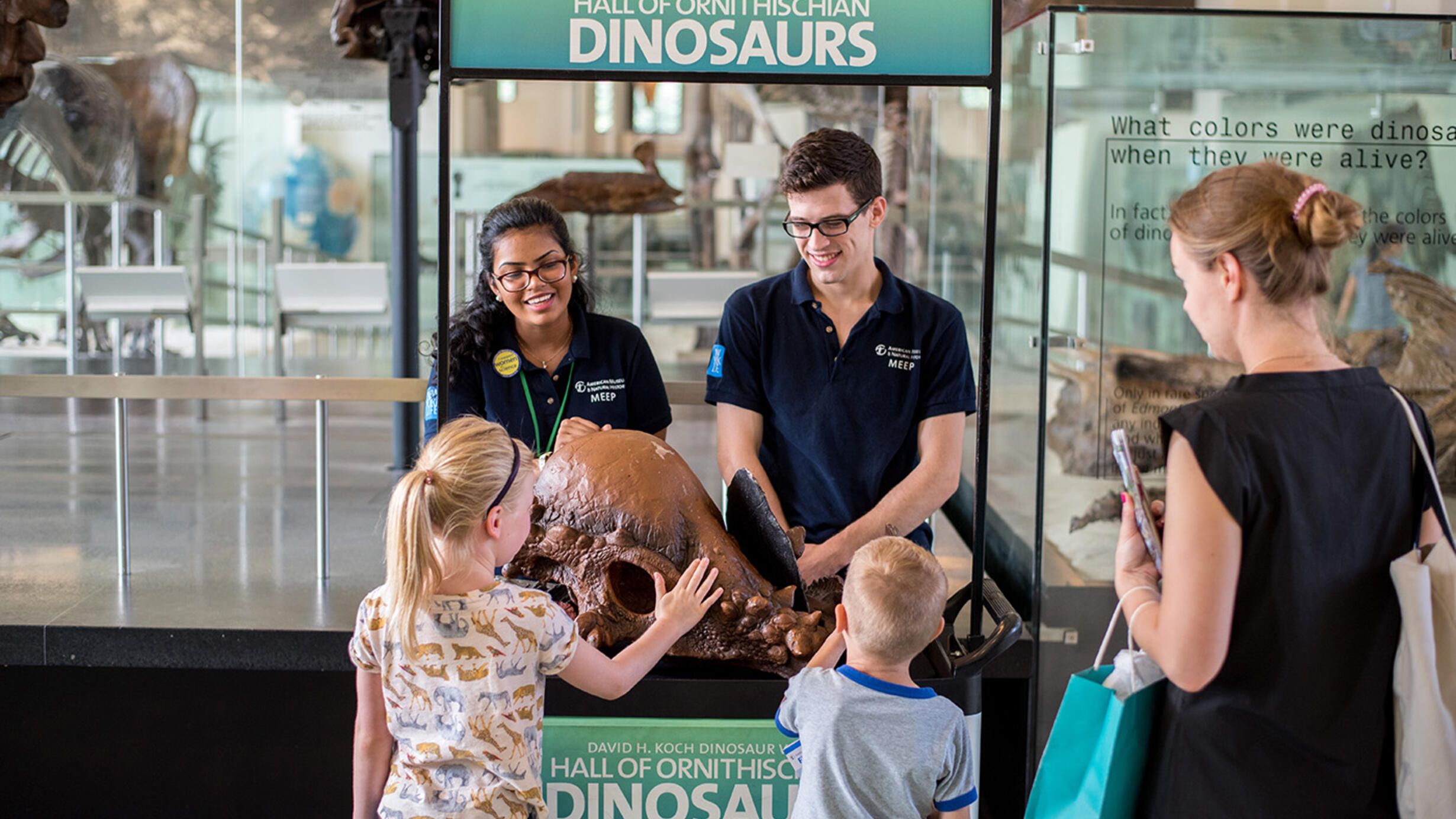Two interns with the Museum Education Employment Program (MEEP) stand behind a booth and show a specimen to two young visitors and their parent.