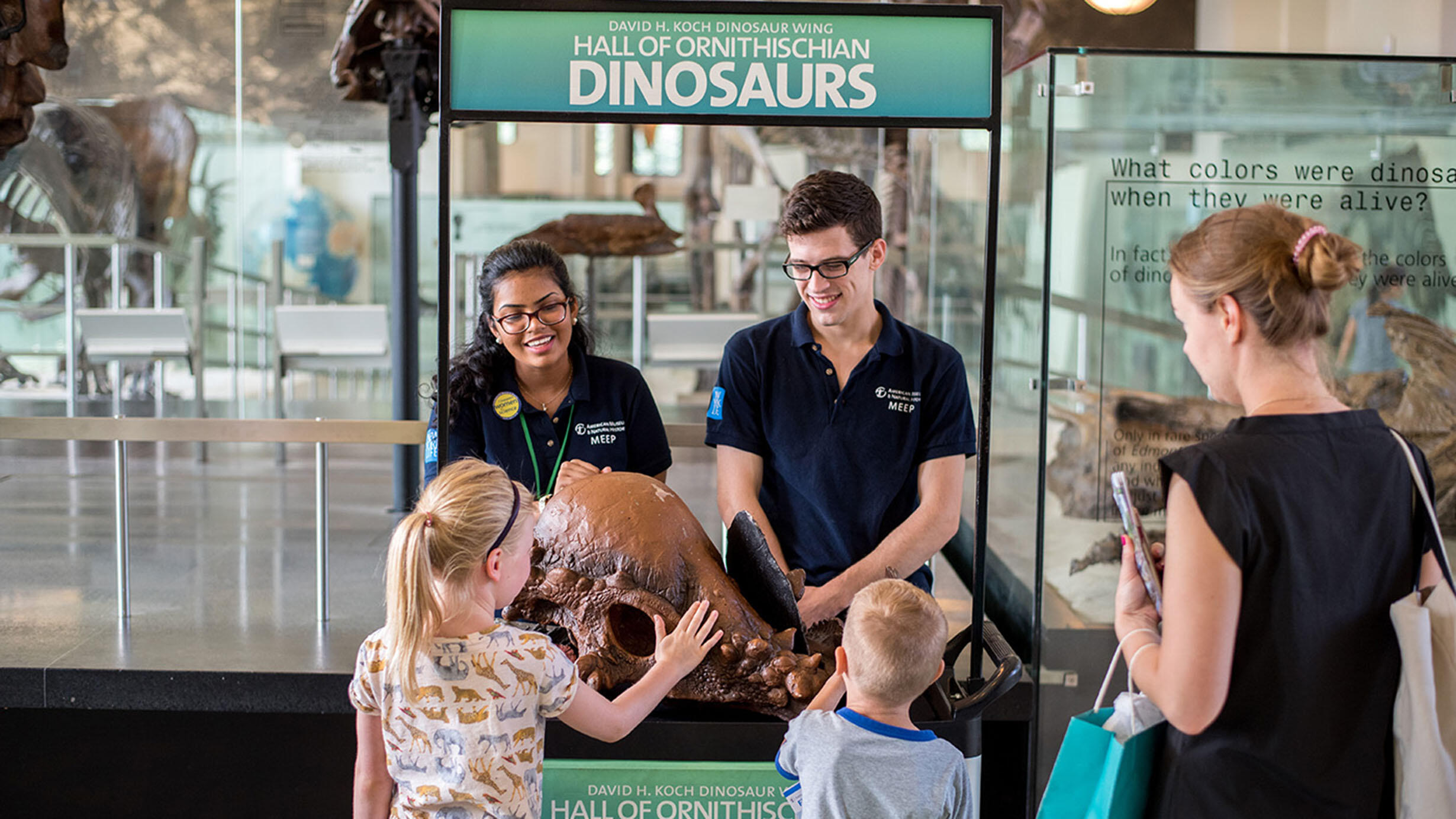 Two interns with the Museum Education Employment Program (MEEP) stand behind a booth and show a specimen to two young visitors and their parent.
