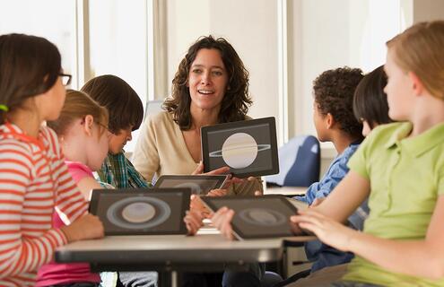 A teacher and her students looking at tablet computers with images of planets