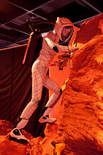 In a traveling exhibition, a model of an astronaut climbing on red-colored rocks wearing a spacesuit called BioSuit, a prototype by MIT professor Dava Newman.