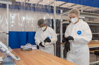 Researchers wear protective suits and masks and put on gloves to prepare to enter the abLab.