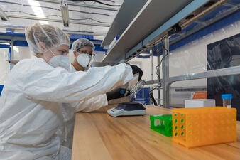 Researchers inside the abLab wear protective gear and weigh specimens on a scale.