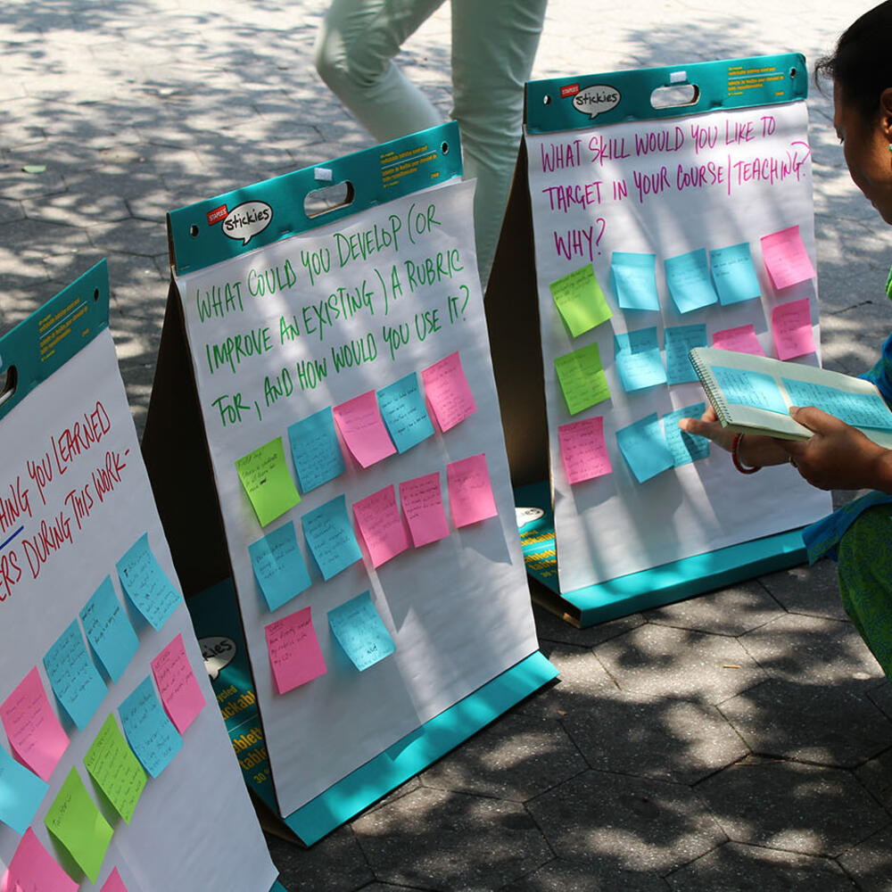 Person bending down to adjust post-it on one of three paper boards covered in post-it notes responding to questions written on each board.