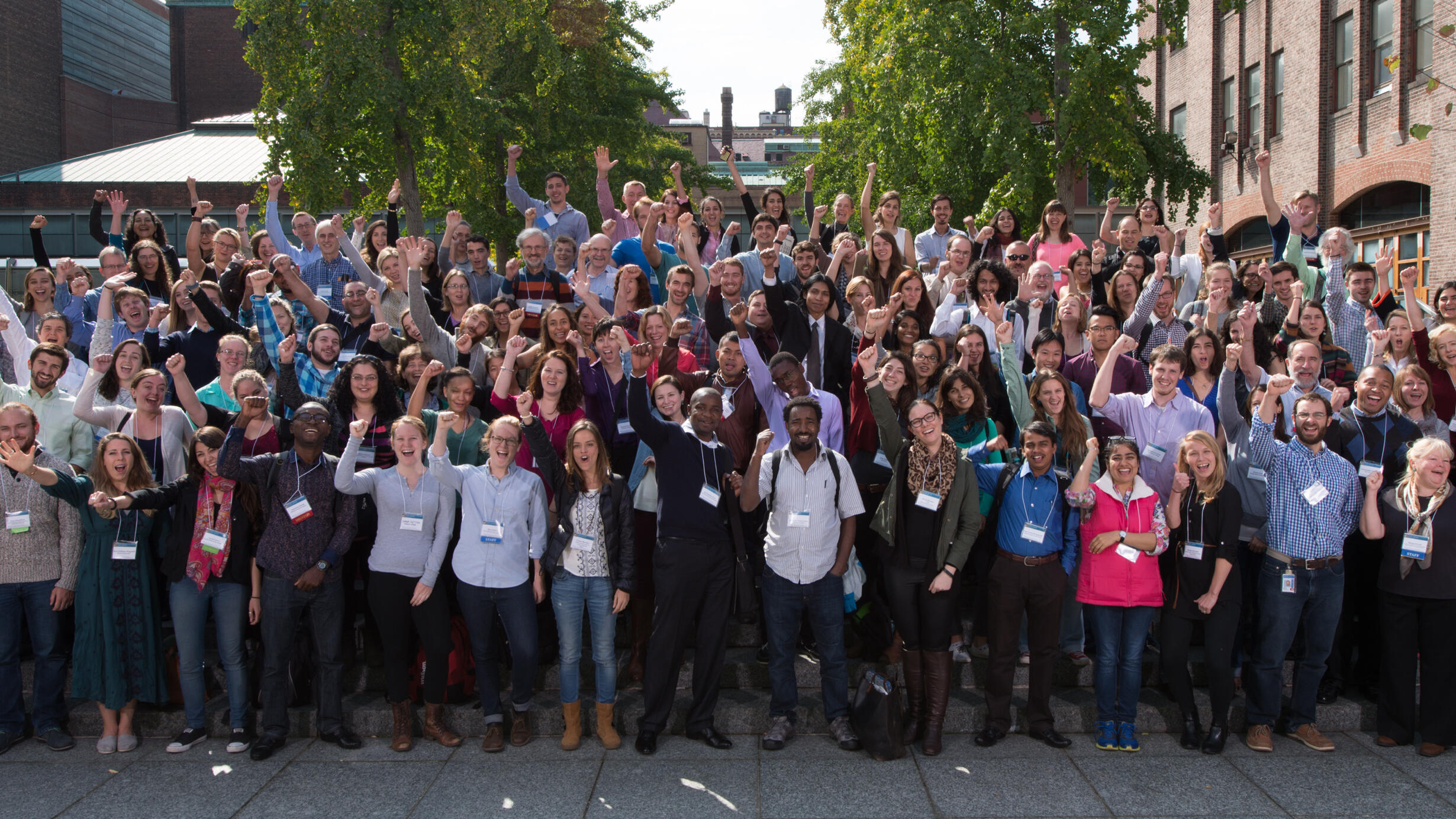 Around 150 Student Conference on Conservation Science participants pose in rows, cheering with their right arms up.