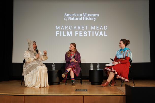 Three speakers in traditional indigenous clothing speak in a panel on stage.