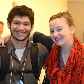 Two people, one wearing a backpack and the other wearing a bright scarf, pose for photo with arms around each other's shoulders.