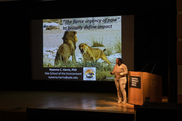 Nyeema Harris stands on stage during her plenary with the slide showing a confrontation between two lions.