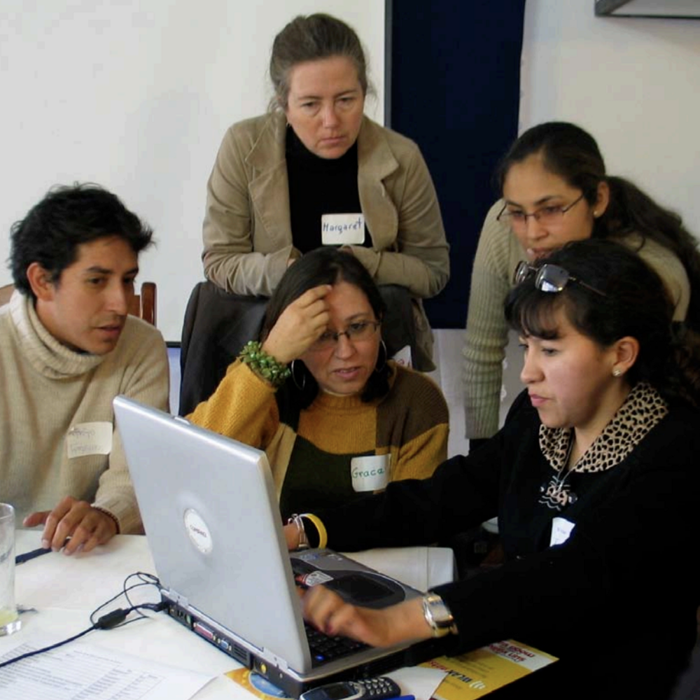 A group of people sit working around a laptop.