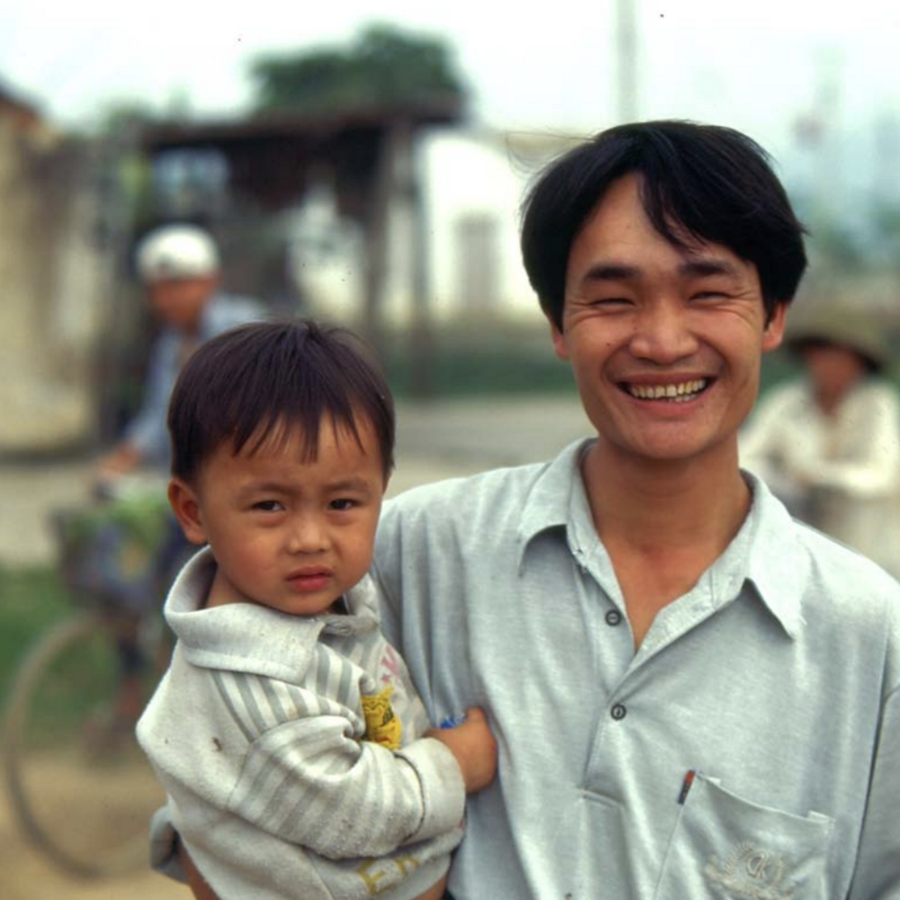 A man smiles while holding a child.