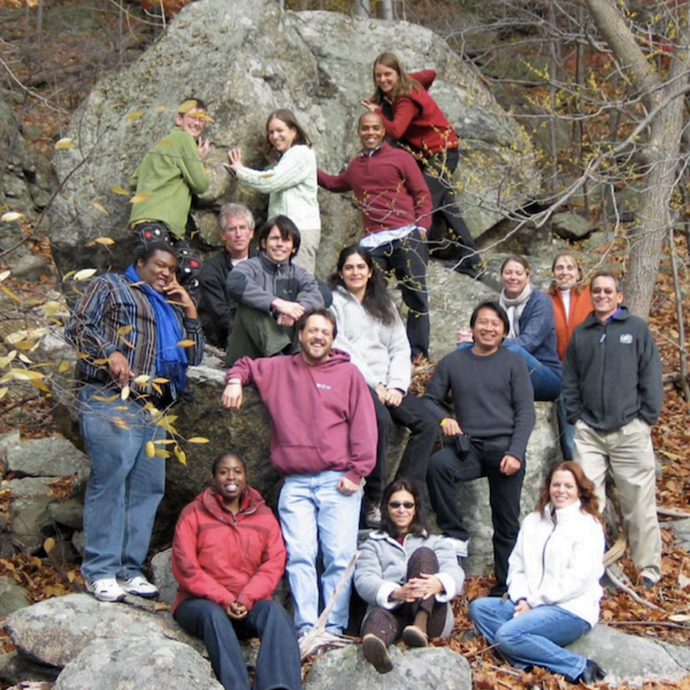 A group of smiling people stands together in the forest.
