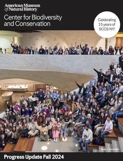 A group of students stand in the Gilder Atrium waving and smiling.