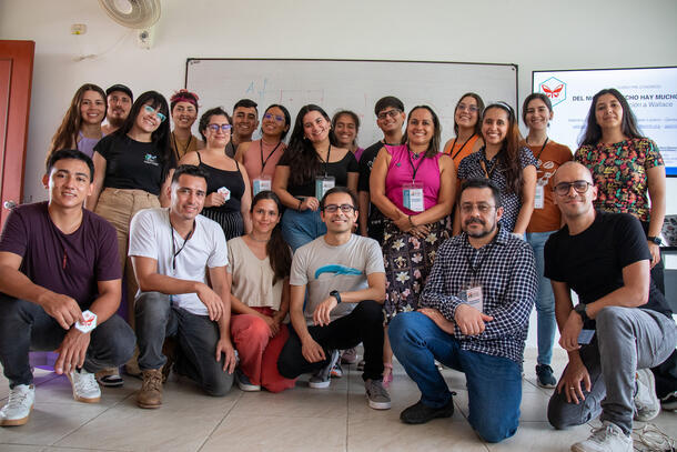 A group of workshop participants pose smiling for the camera in front of a white board in a classroom.