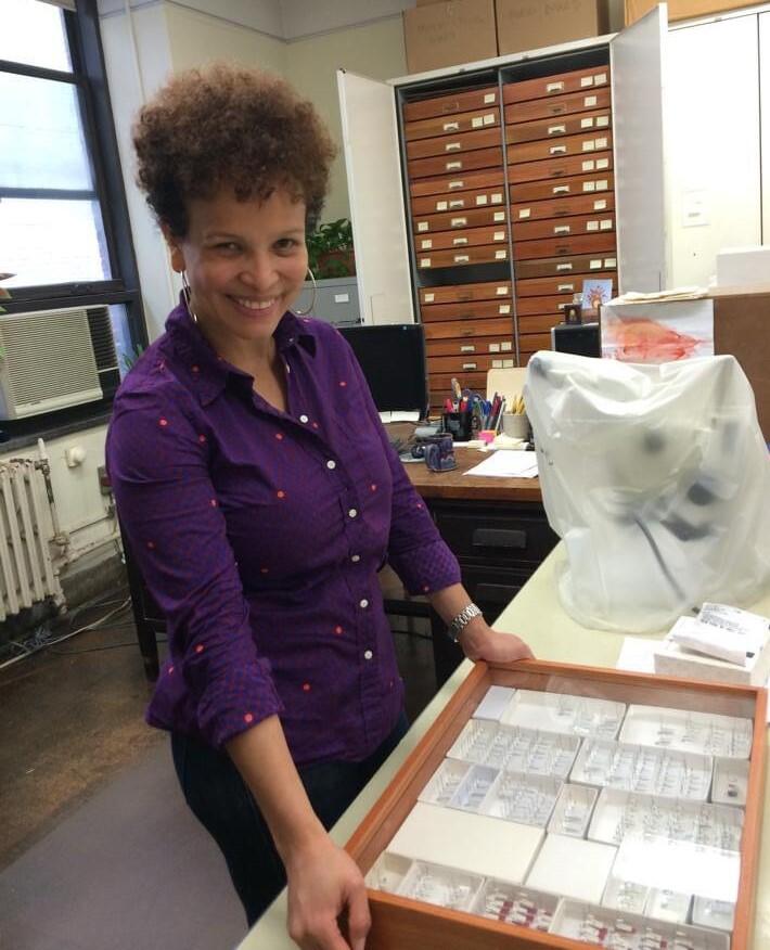 Scientist Ruth Salas stands in front of a table with a glass case full of small pinned specimens.