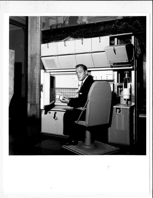 Press release photograph showing Joseph M. Chamberlain in the kitchen of the ARIES space laboratory in the Man in Space exhibit, 1961