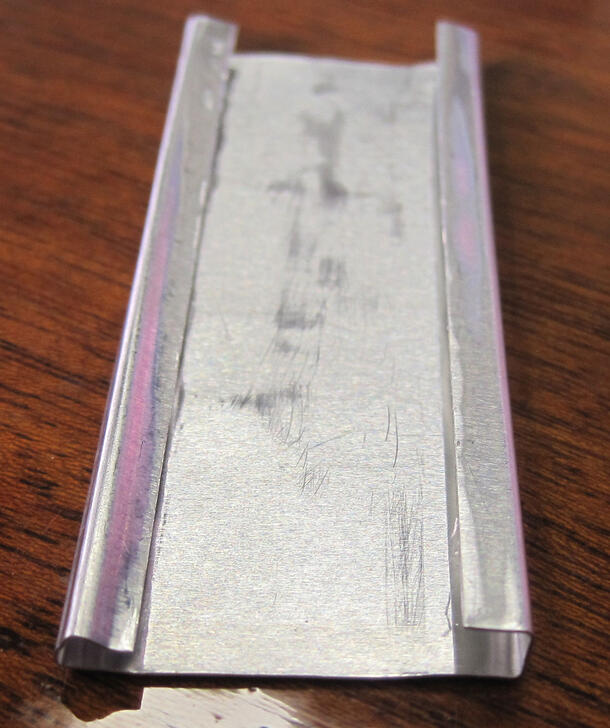 A small long rectangular sheet of aluminum with two curled over edges used to hold a slide.